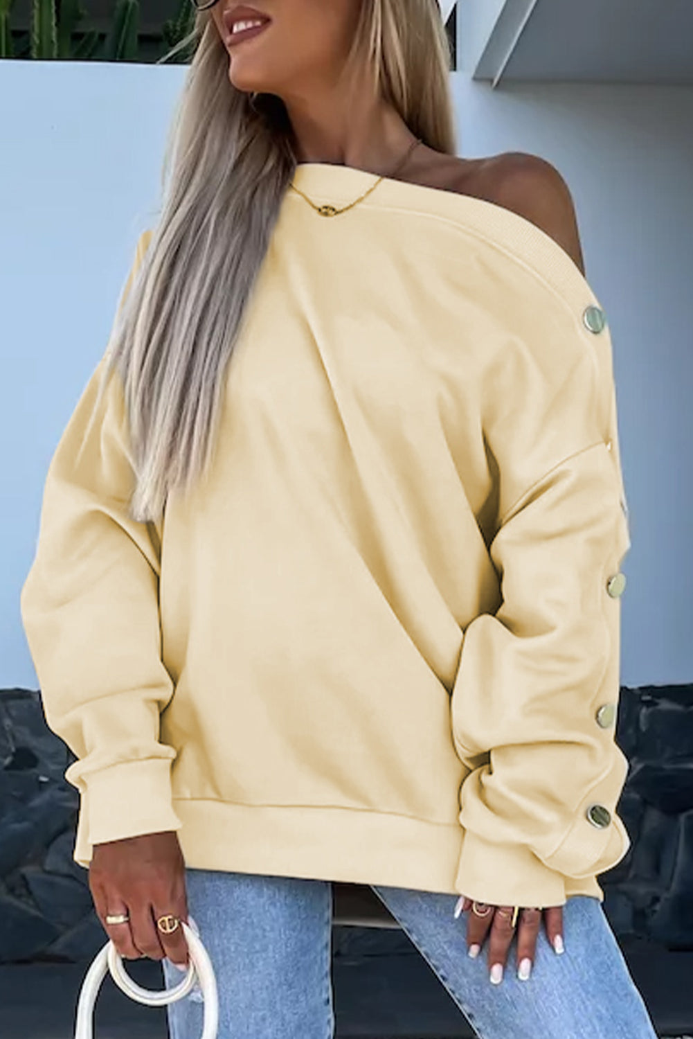 Woman with long wavy hair wearing the Beige Buttoned Sleeve Dropped Shoulder Sweatshirt, standing in a bright indoor setting.