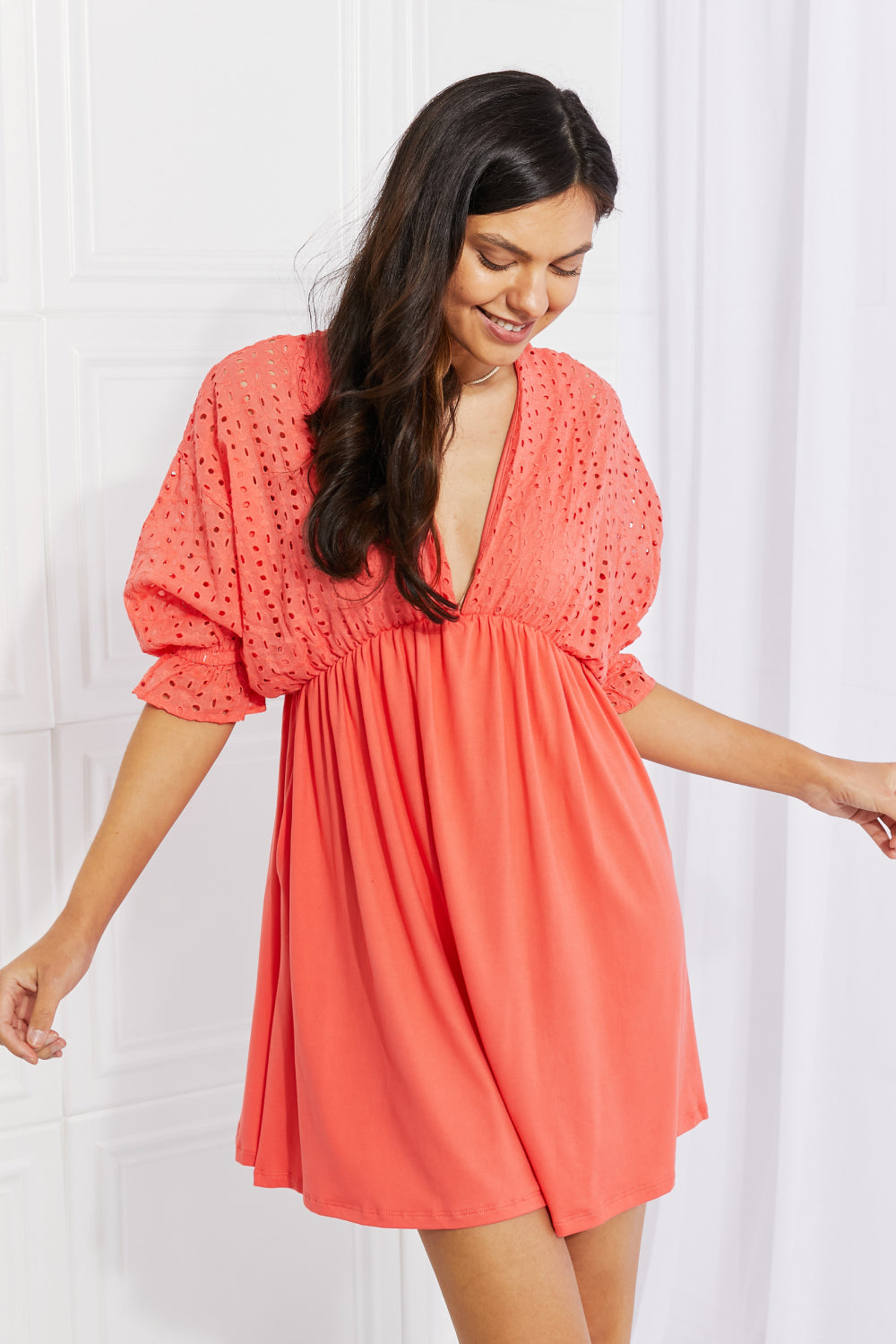 A person wearing the Ninexis Everyday Dreams Eyelet Contrast Dress, characterized by a romantic-style with an orange hue, featuring an eyelet-textured top and a flowing skirt, stands against a white background.