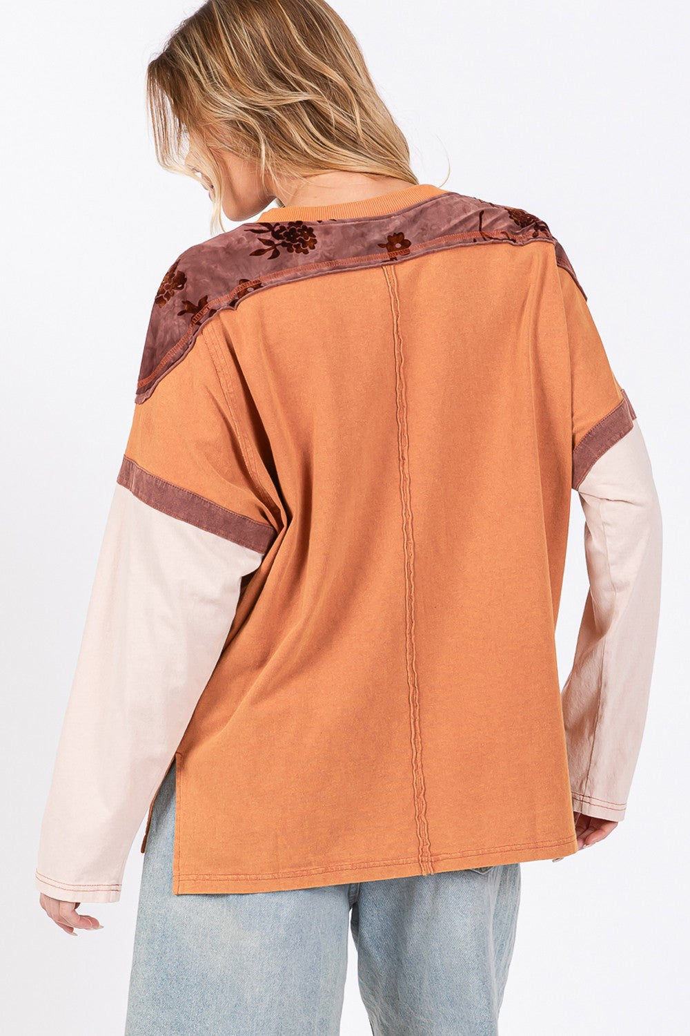 A person wearing a beige hat, a SAGE + FIG Star Patch Long Sleeve Color Block T-Shirt in orange, and light blue jeans stands against a plain background.