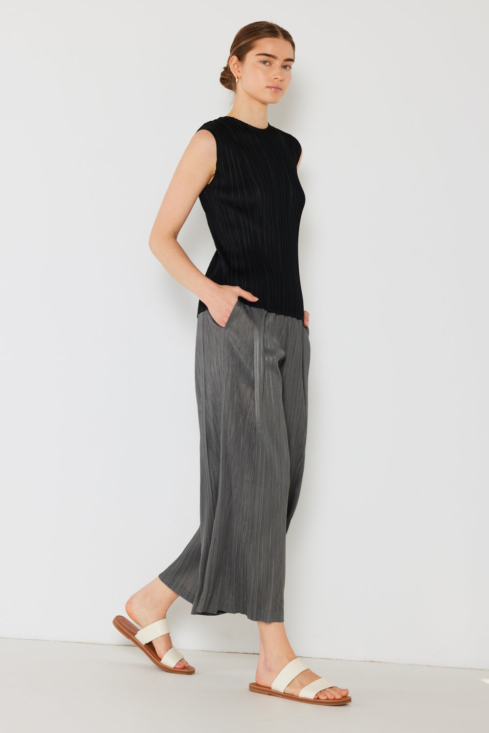 A person wearing the Marina West Swim Pleated Wide-Leg Pants with side pleat detail in red, standing against a white background with hands in pockets and wearing white sandals.