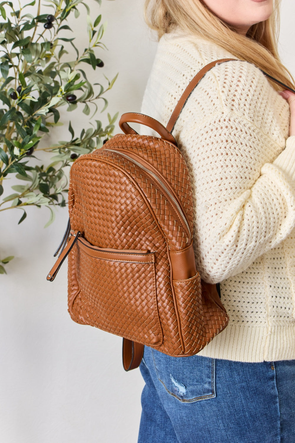 A person wearing a cream sweater and blue jeans carries the SHOMICO PU Leather Woven Backpack, showcasing exquisite craftsmanship with its woven design.