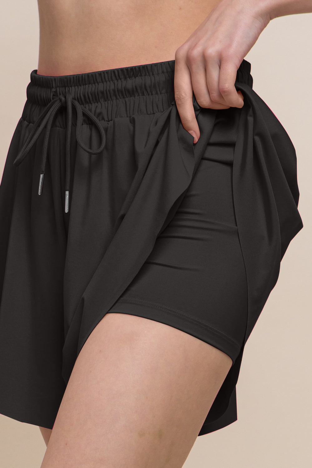 Person adjusting the drawstring waist of Love Tree Two In One Drawstring Active Shorts in black against a neutral background.