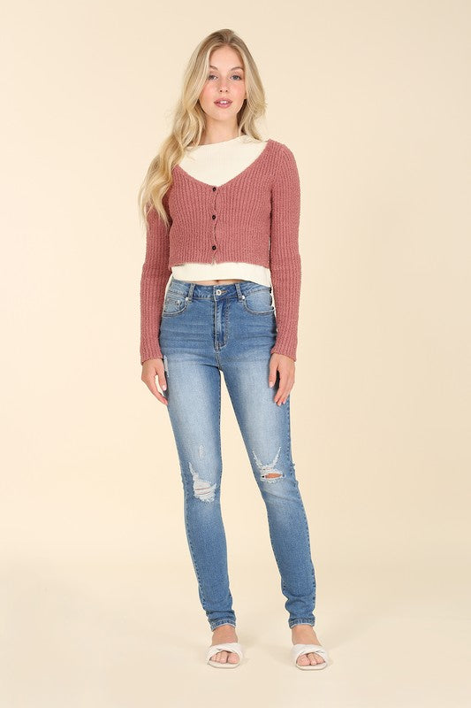 Someone wearing a sleeveless top and Dark Wash Distressed Skinny Jeans is kneeling on a white chair against a beige background.