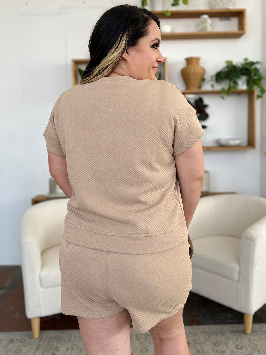 A woman with long dark hair is wearing the Double Take Full Size Texture Short Sleeve T-Shirt and Drawstring Shorts Set, made from beige polyester. The set features a short-sleeve top and matching shorts, with the woman standing confidently with one hand in her pocket and maintaining a neutral expression. For easy care, remember to machine wash cold.