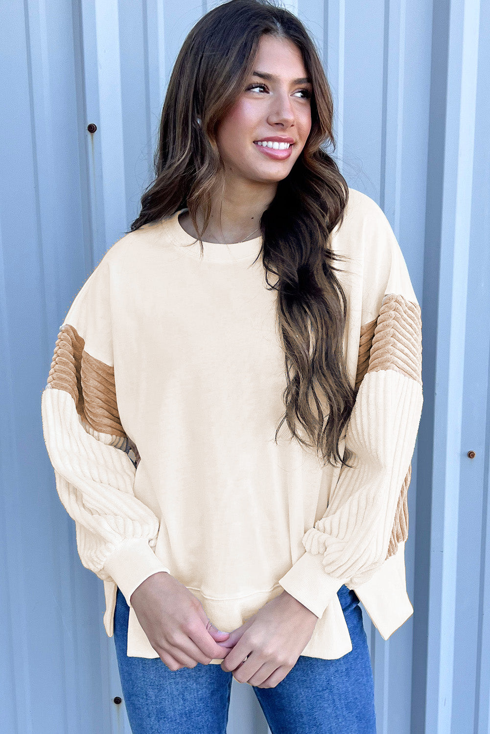 A person with long hair is wearing an Apricot Corduroy Patchwork Drop Shoulder Long Sleeve Sweatshirt, standing with their back to the camera against a light blue corrugated metal wall.