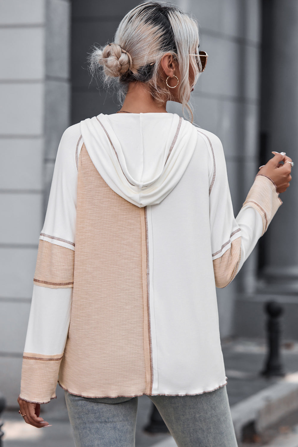 A person with light blonde hair in a bun, wearing sunglasses and a Multicolor Colorblock Seamed Ribbed Henley Hoodie, is walking outside on a paved street.