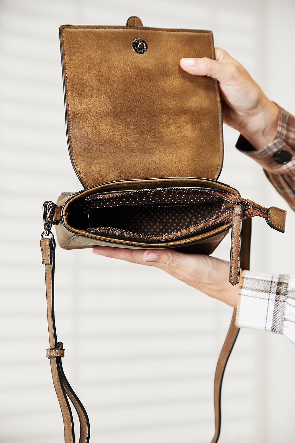 A person wearing a dark sweater and jeans holds the SHOMICO PU Leather Crossbody Bag, a stylish accessory in orange-brown featuring a flap and buckle detail.