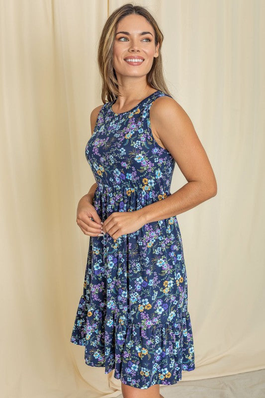 A person wearing the Sleeveless Botanical Floral Tiered Dress poses gracefully in front of a pink curtain.