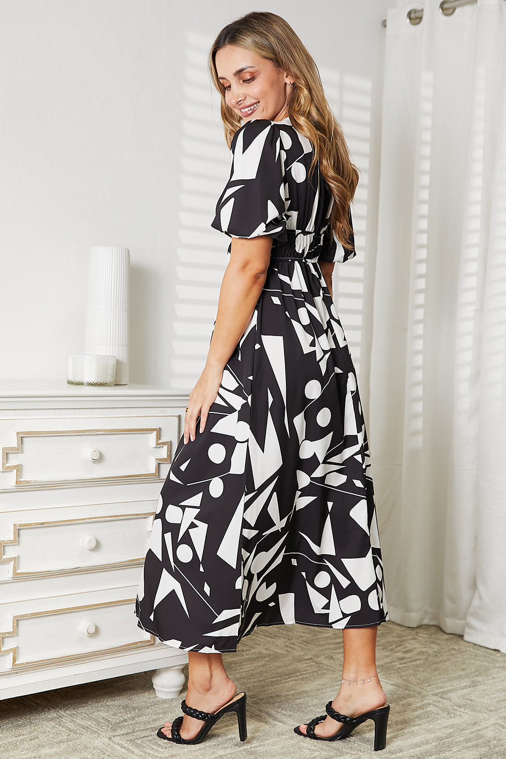 A person in a Printed Surplice Balloon Sleeve Dress stands near a brown chair and a round table with a potted plant.