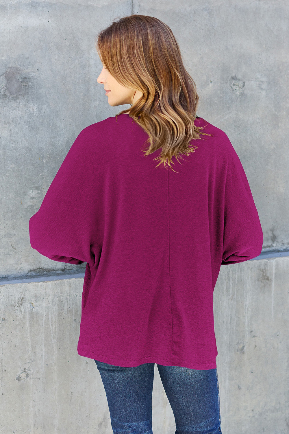 A person wearing a Double Take Full Size Round Neck Long Sleeve T-Shirt in green, blue distressed jeans with a slightly stretchy fit, and a crossbody bag, holding a beverage in a plastic cup.