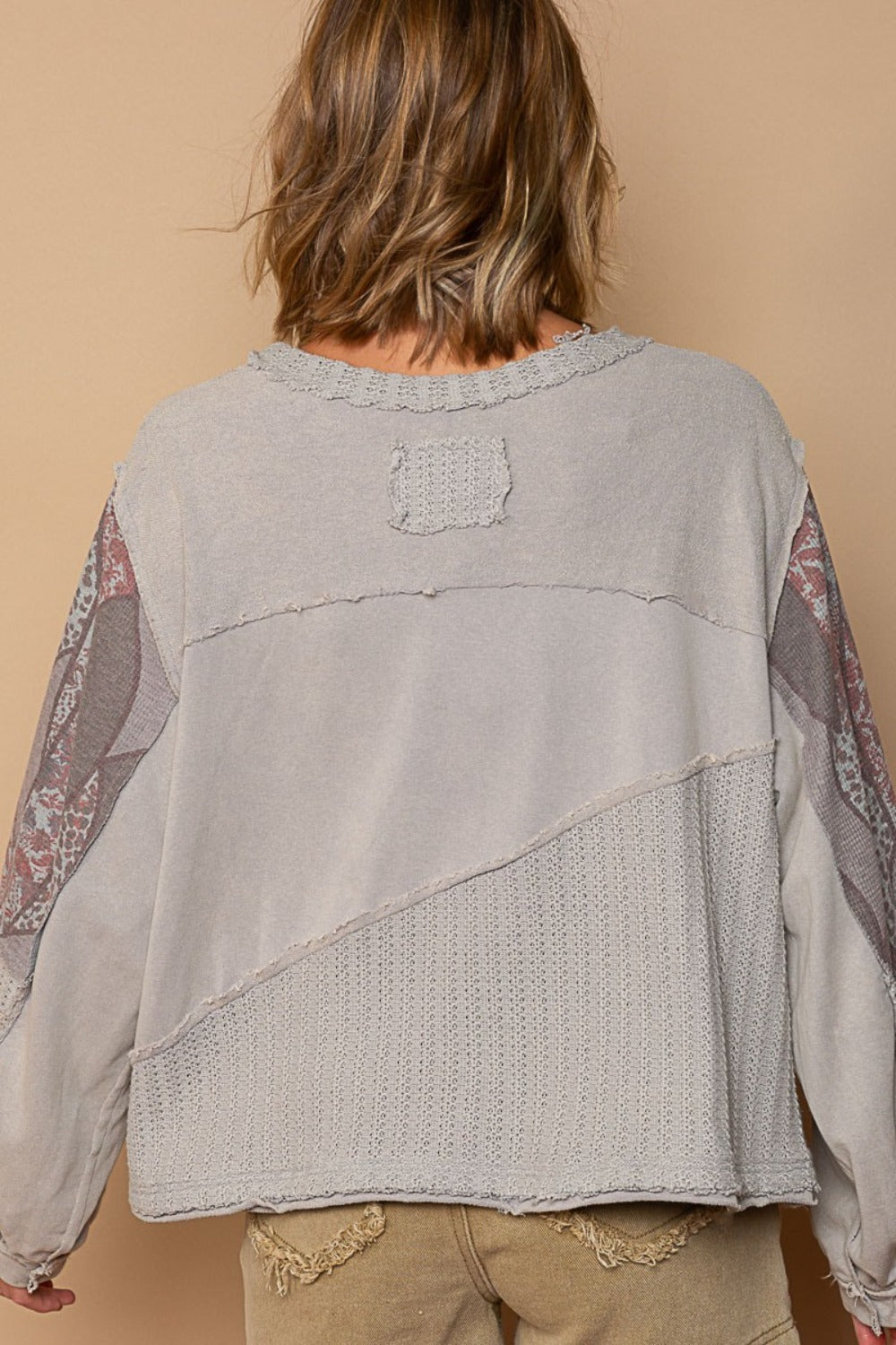 Young woman wearing a POL Long Sleeve Cut Sew Peace Emblem Top featuring a large peace sign design paired with beige shorts, standing against a plain background.