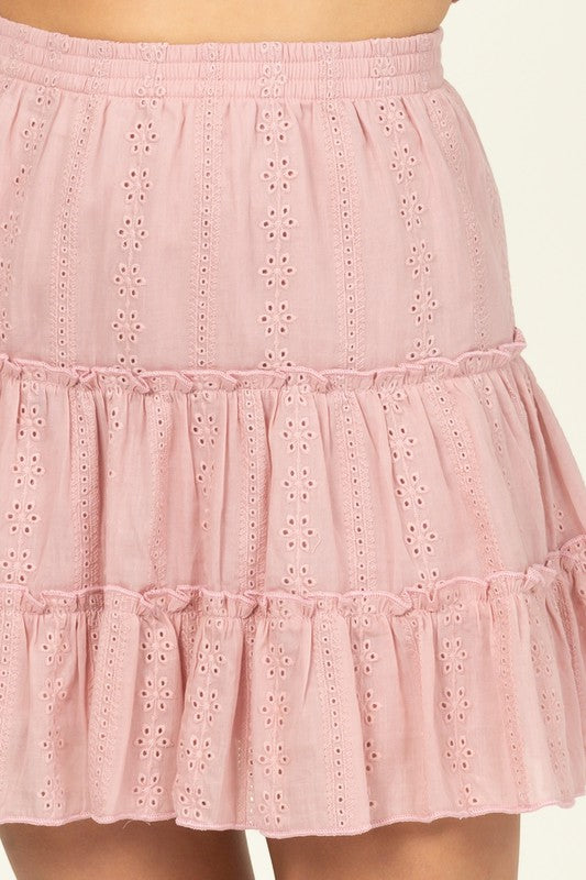 A person wearing the Forever Classy High Waist Tiered Mini Skirt in pink, featuring eyelet details and a ruffled design.