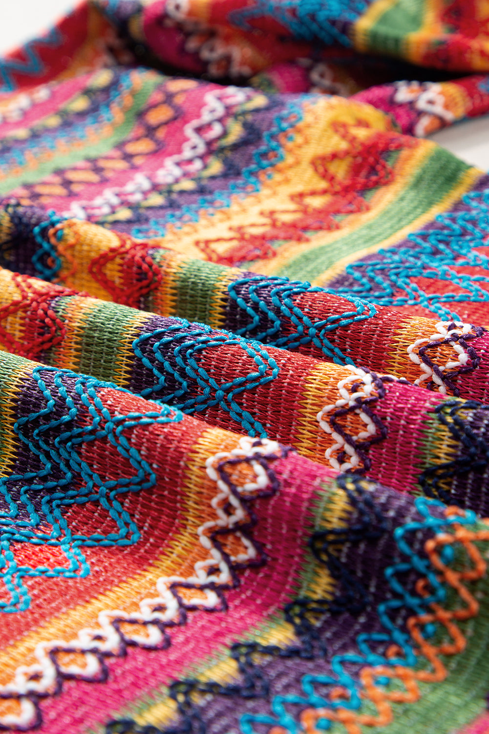 A person stands with hands in the pockets of their denim shorts, wearing a colorful Rose Red Ethnic Wavy Pattern Drop Shoulder Knit Top and a white shoulder bag.