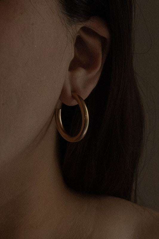 The Canal Hoop Earrings, with their lustrous 14k gold plating, are artfully displayed on a white background, highlighting their hypoallergenic allure.