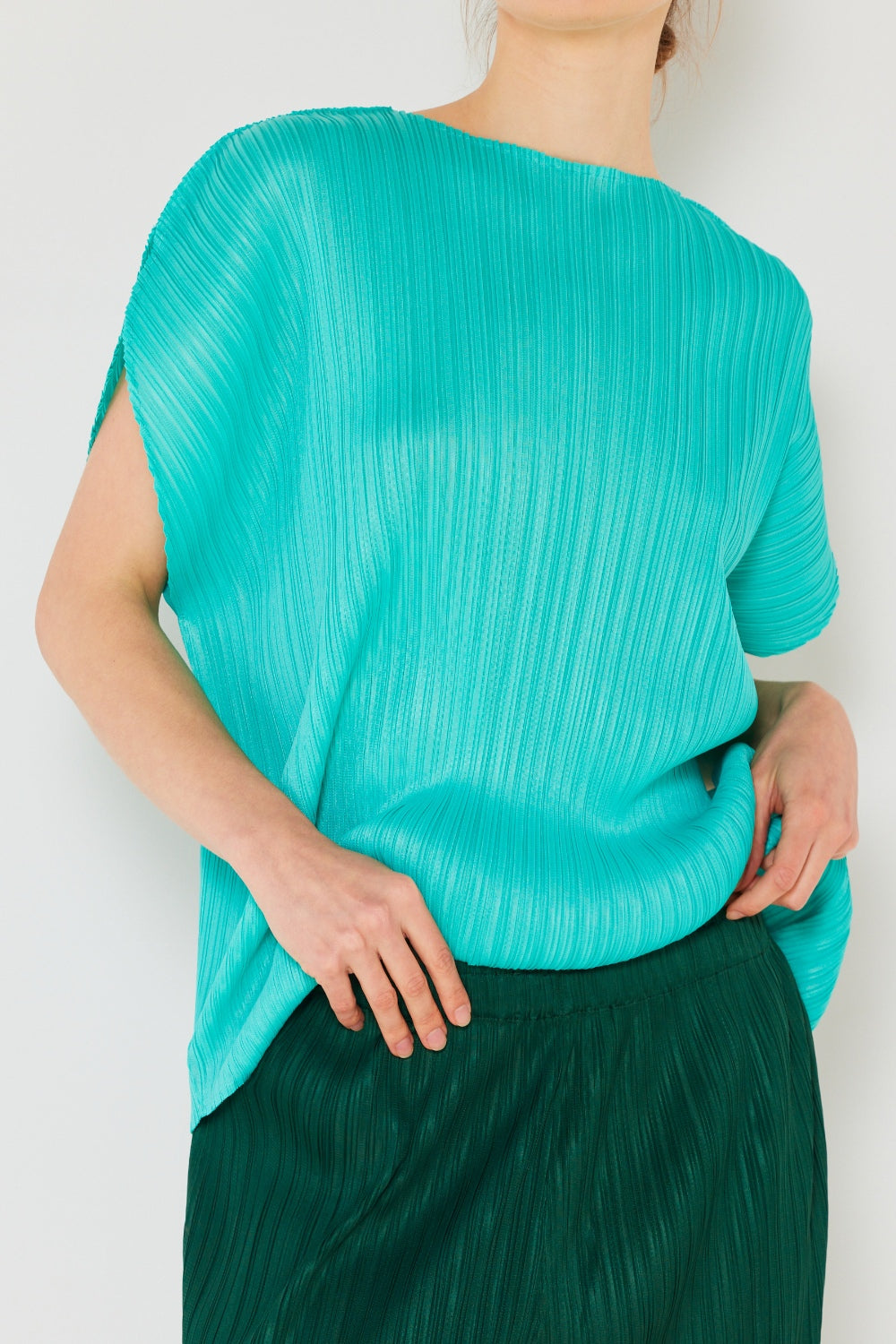 A person wearing the Marina West Swim Rib Pleated Oversized Dolman Sleeve Top in a fashionable light blue shade, paired with a brown belt and black skirt, stands against a plain background.