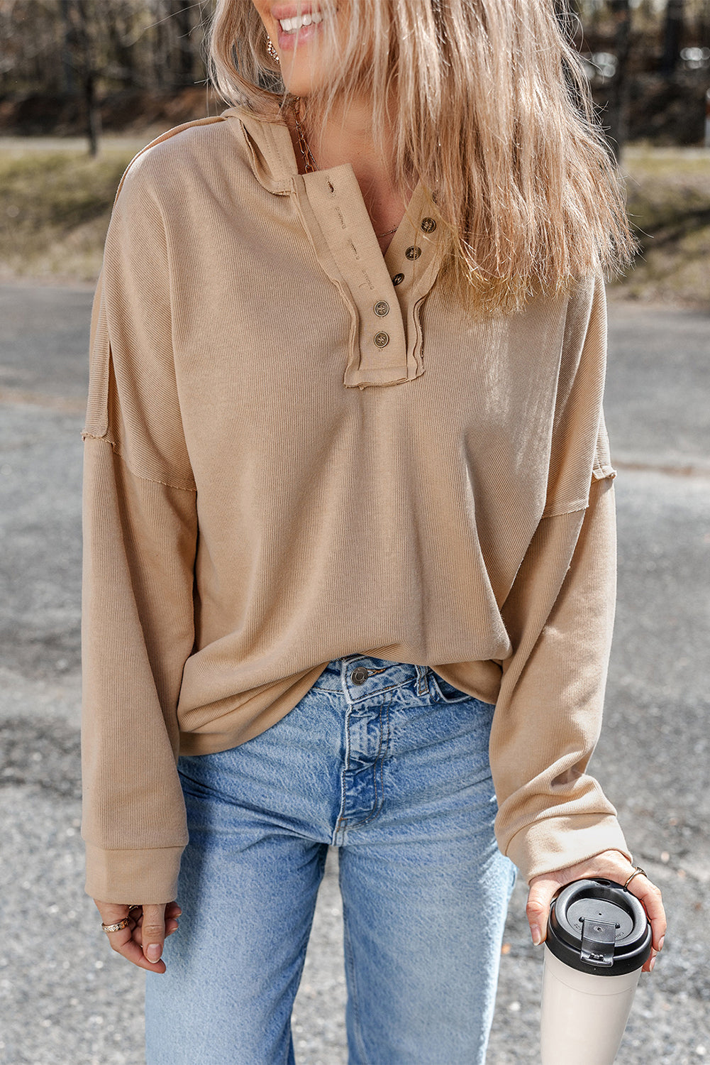 Person wearing a Khaki Casual Button Solid Patchwork Trim Hoodie and blue jeans is standing outdoors holding a white tumbler. The individual's blonde hair is partially visible from behind.