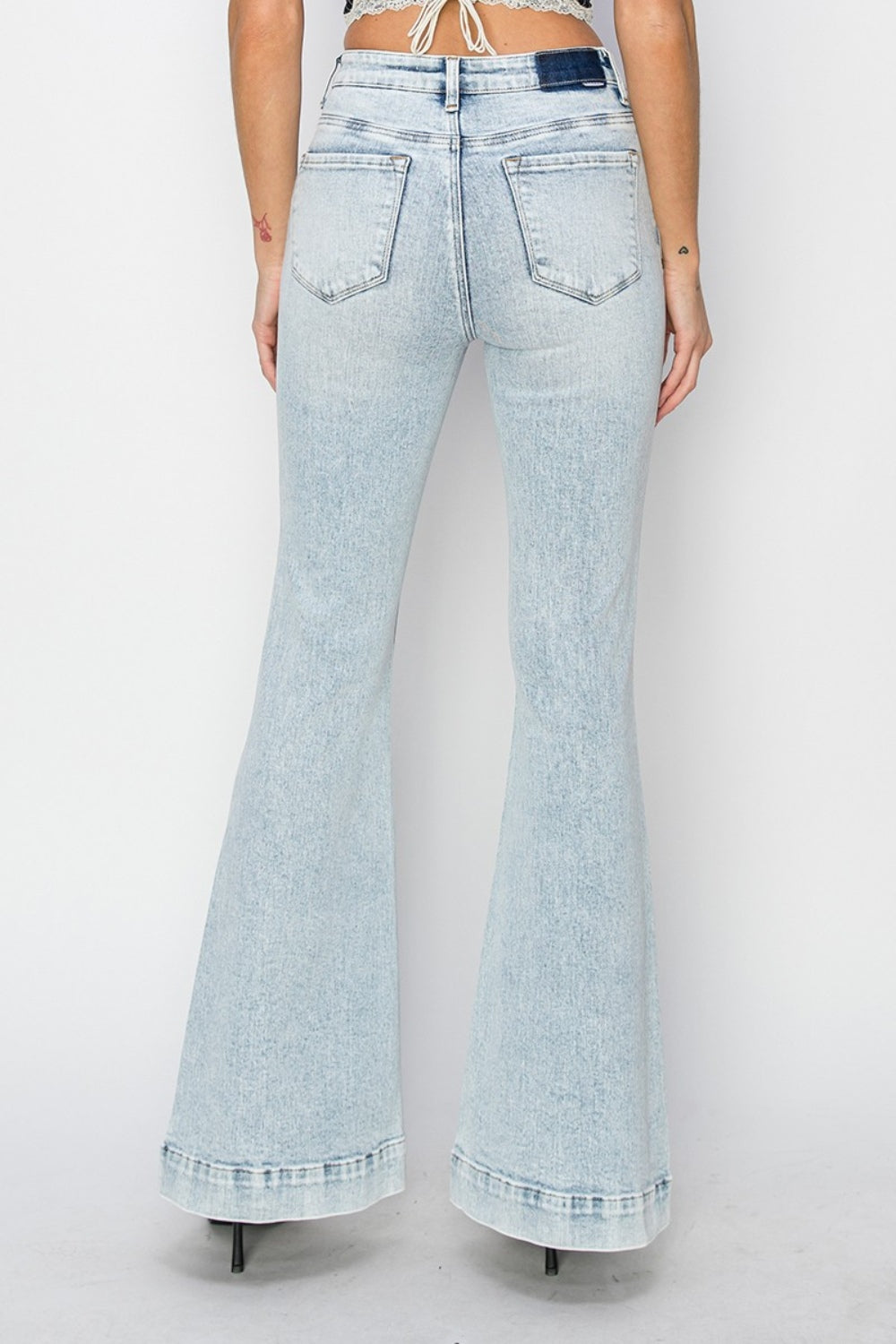 A person wearing Risen Full Size High Rise Front Patch Pocket Flare Jeans in a light wash, paired with black strappy sandals, stands against a white background.