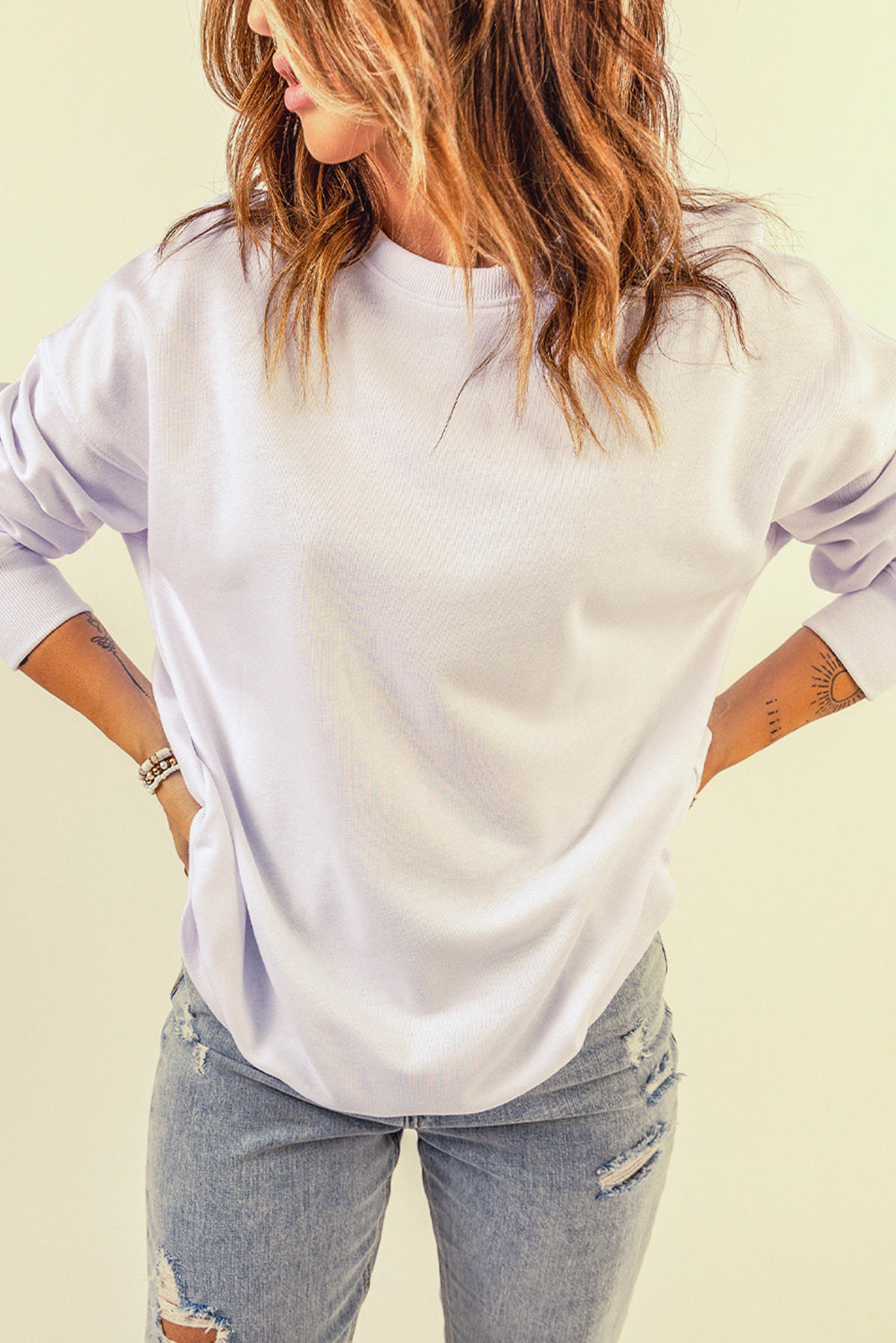 A person wearing a White Oversized Solid Drop Shoulder Sweatshirt and distressed blue jeans is shown from the back, with wavy, shoulder-length hair.