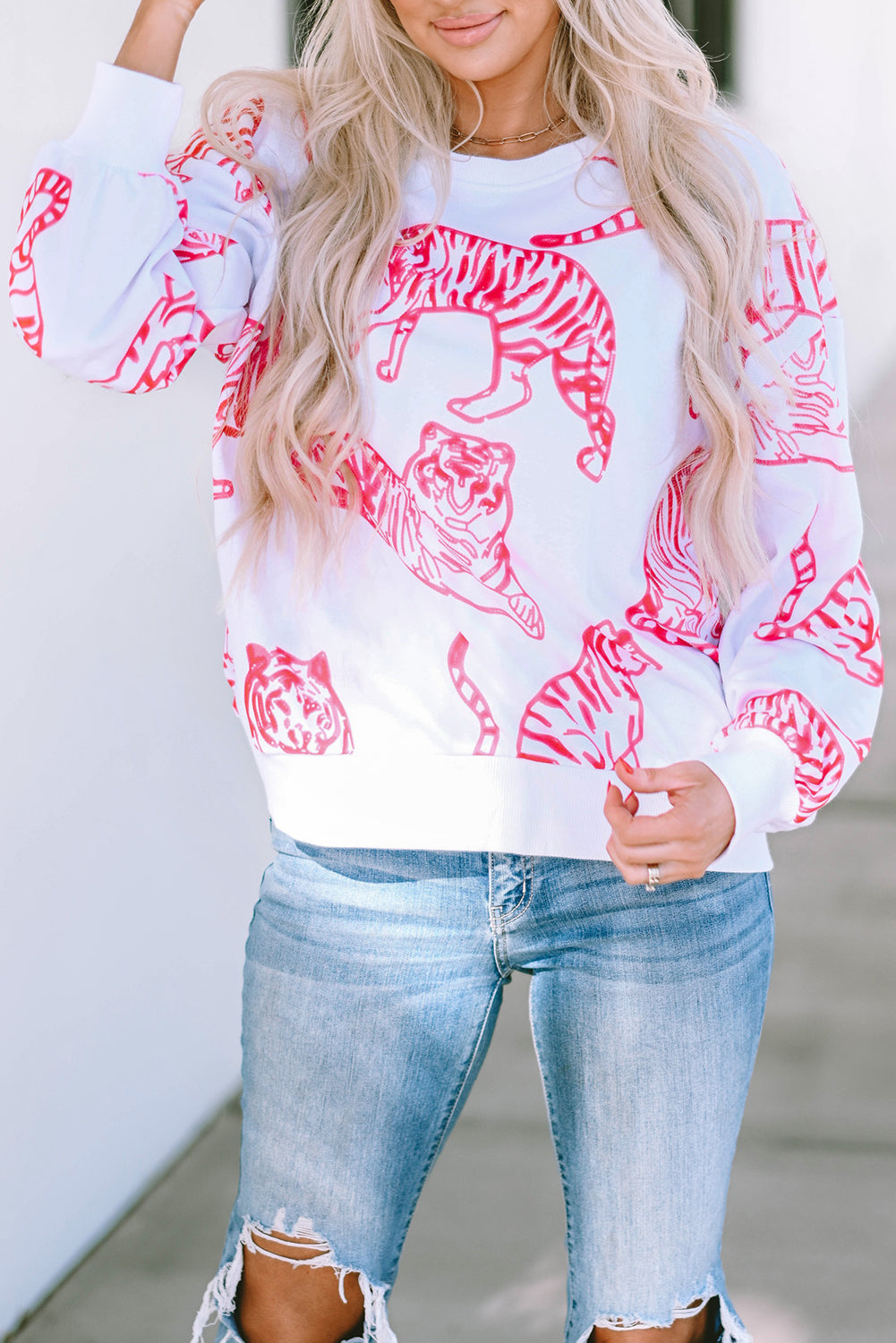 A person with long blonde hair wears a trendy Bright White Pink Animal Print Pullover Sweatshirt, paired with blue jeans, standing outdoors with their back facing the camera.