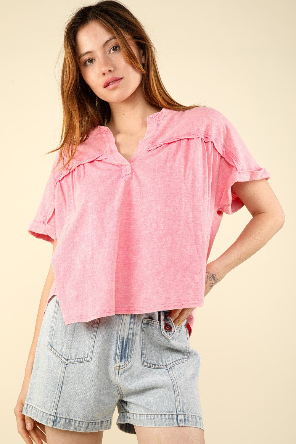 A woman in a casual fit with a VERY J Notched Short Sleeve Washed T-Shirt and light denim shorts stands against a plain background, capturing the essence of everyday wear.