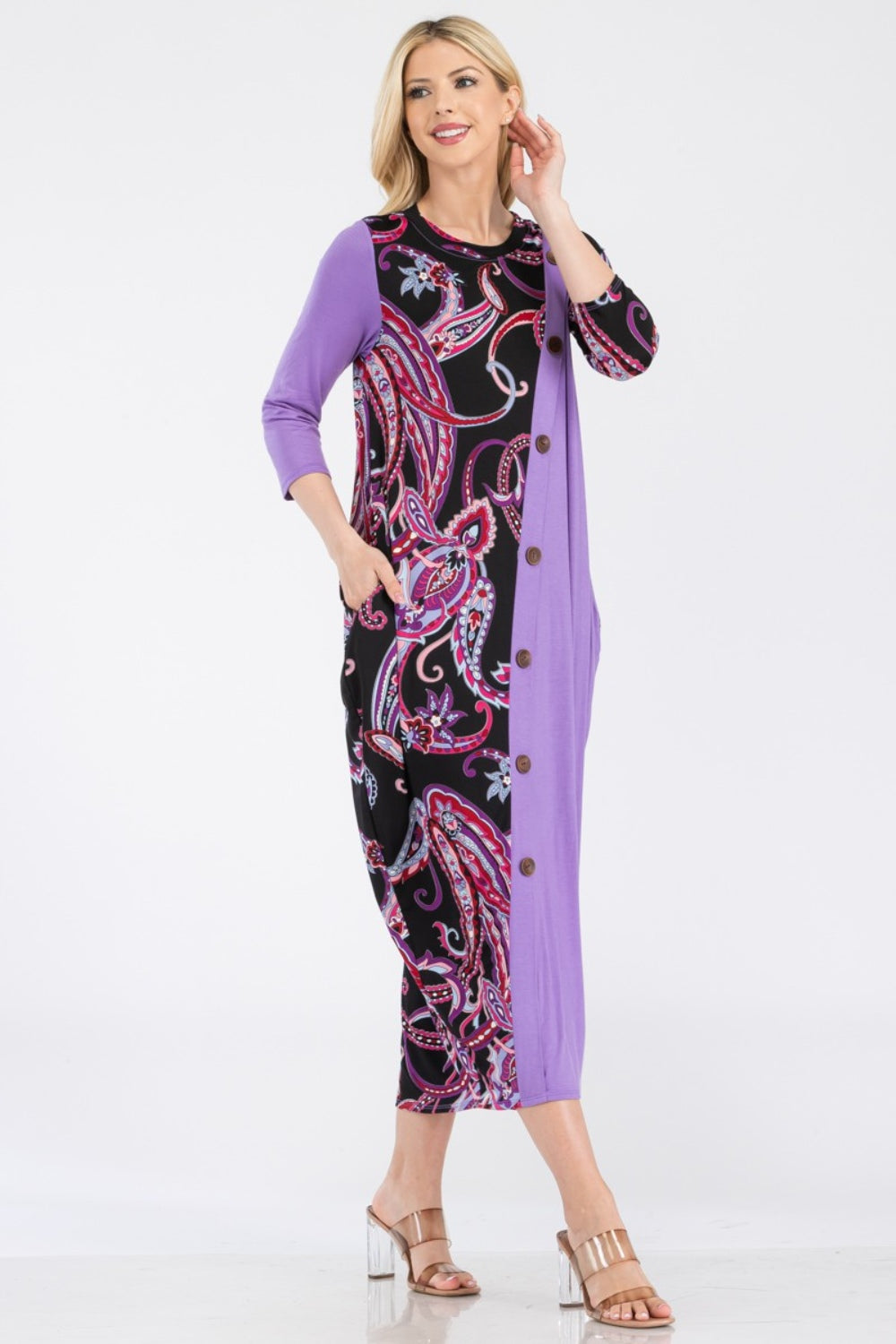 A woman wearing the Celeste Full Size Paisley Contrast Midi Dress with pockets, showcasing a versatile purple and black paisley print, button front detail, and long sleeves.