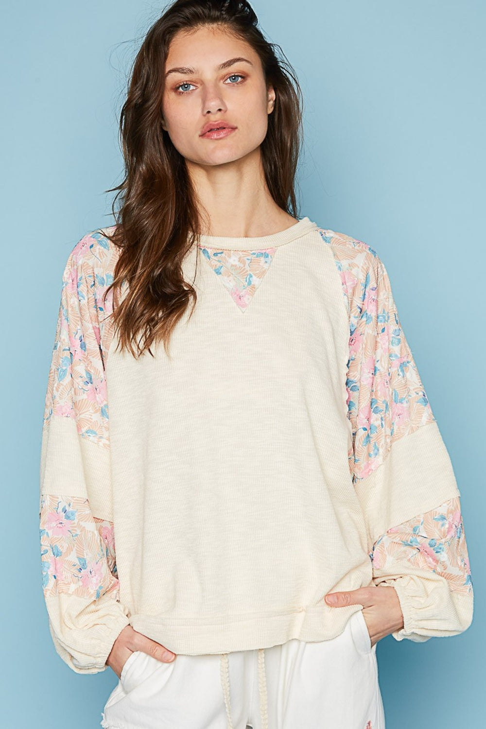 A woman wearing a POL Round Neck Balloon Floral Long Sleeve Top stands against a blue background.