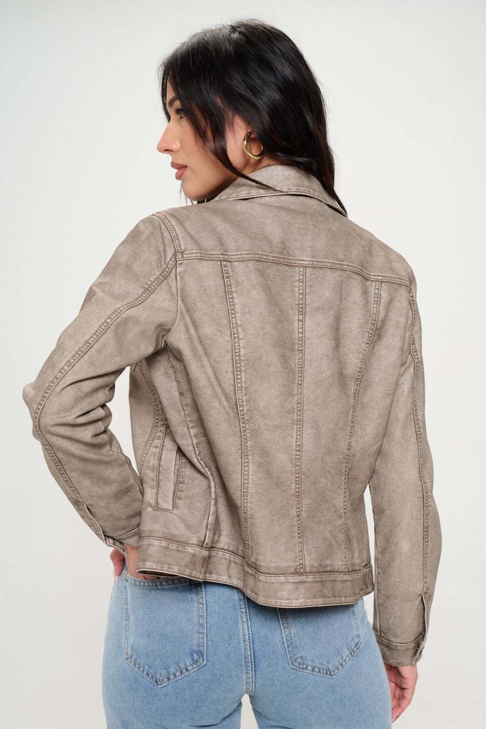 A woman with long dark hair wears a Coalition LA Button Down Cargo Vegan Leather Shacket in light beige over a ribbed top and blue jeans, standing against a light background.