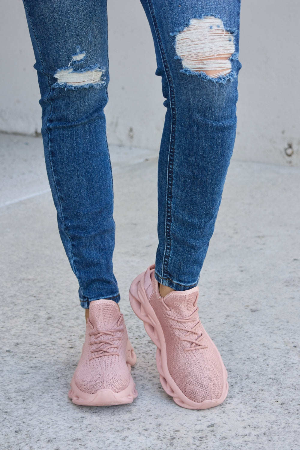 Person wearing blue ripped jeans and Forever Link Mesh Breathable Platform Athletic Shoes in light pink, standing on a concrete surface.