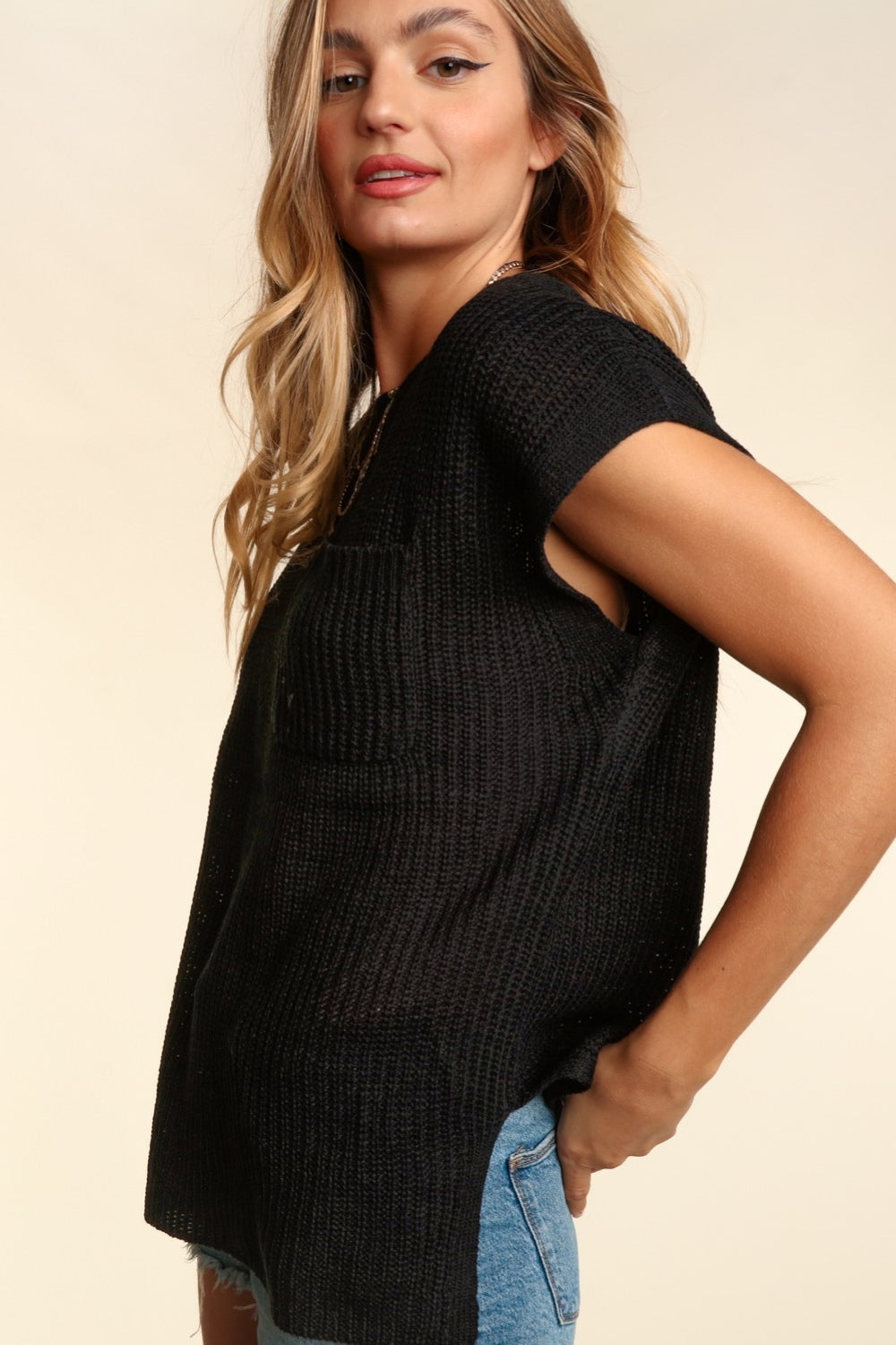 A person with long hair, wearing a Haptics Pocketed Round Neck Cap Sleeve Knit Top and denim shorts, is smiling against a neutral background.