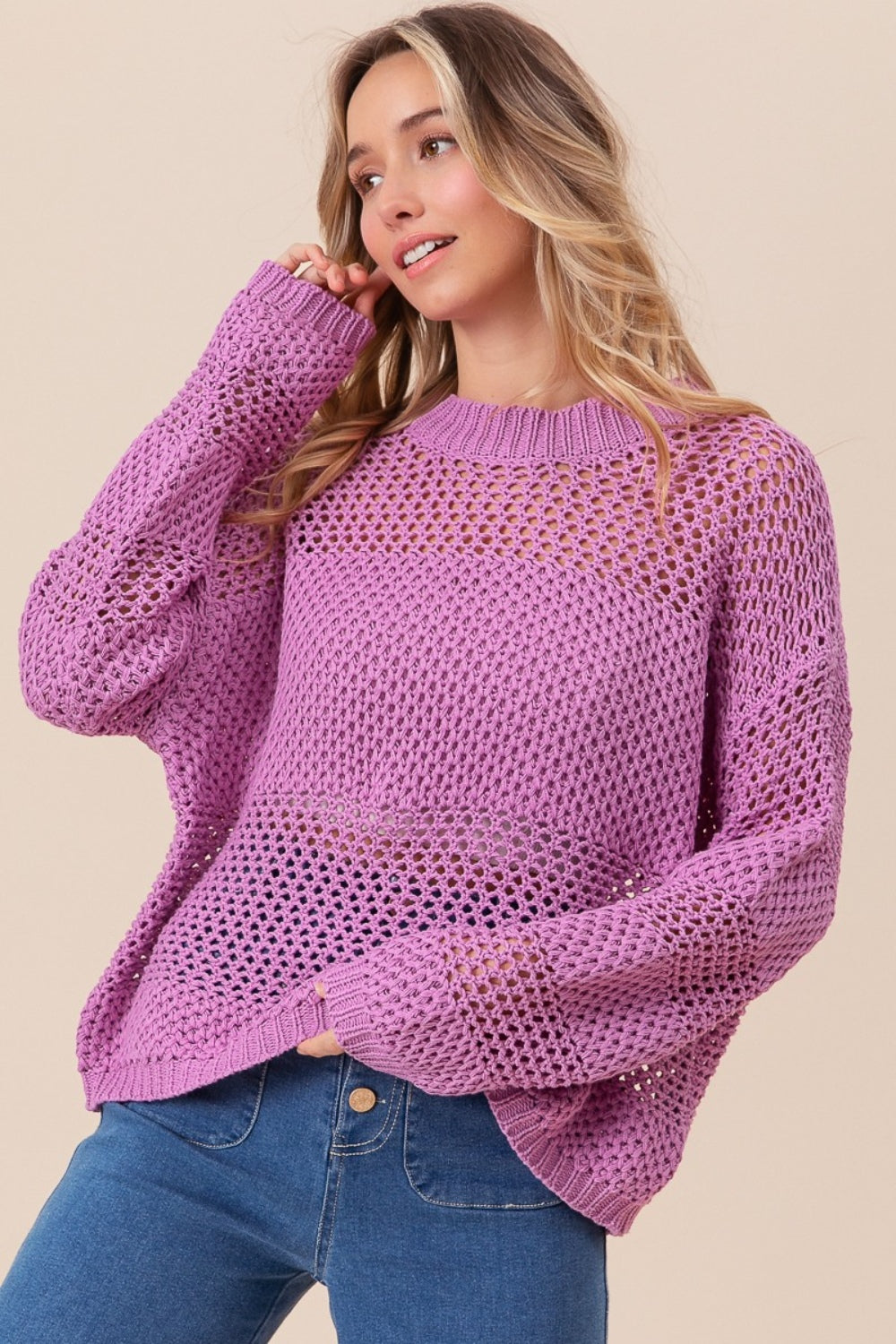 Wearing the BiBi Openwork Long Sleeve Knit Top in purple and blue jeans, a person smiles slightly while gazing to the side, exuding a fashion-forward vibe.