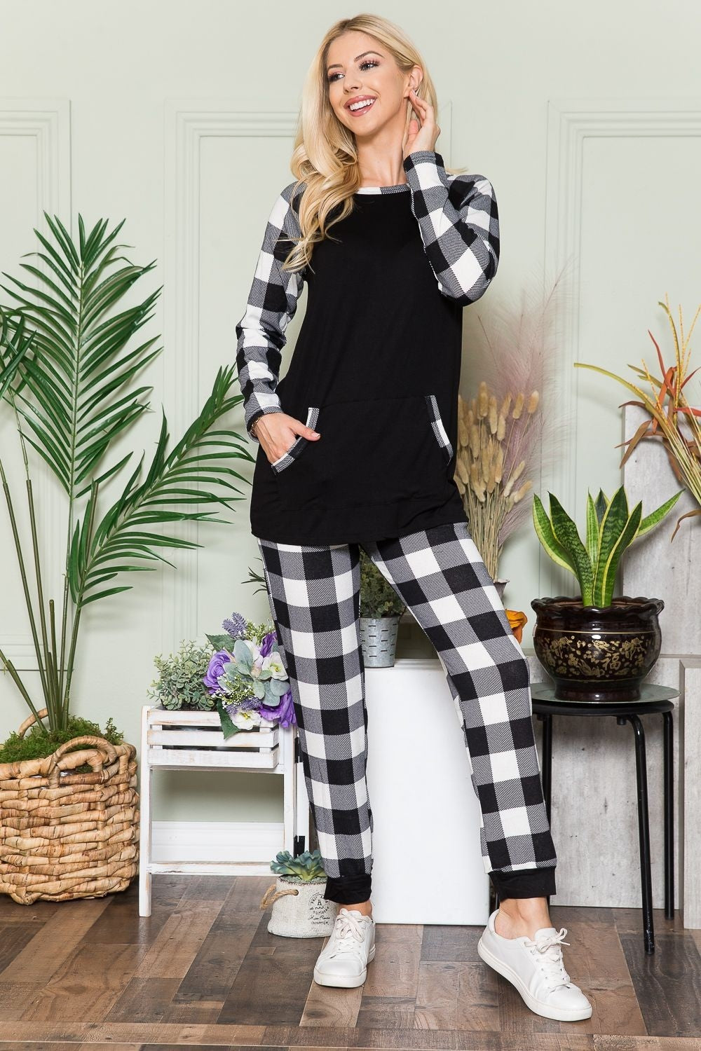 A person wearing the Celeste Plaid Long Sleeve T-Shirt with Pockets stands in a room filled with plants and wooden flooring, presenting a laid-back style.