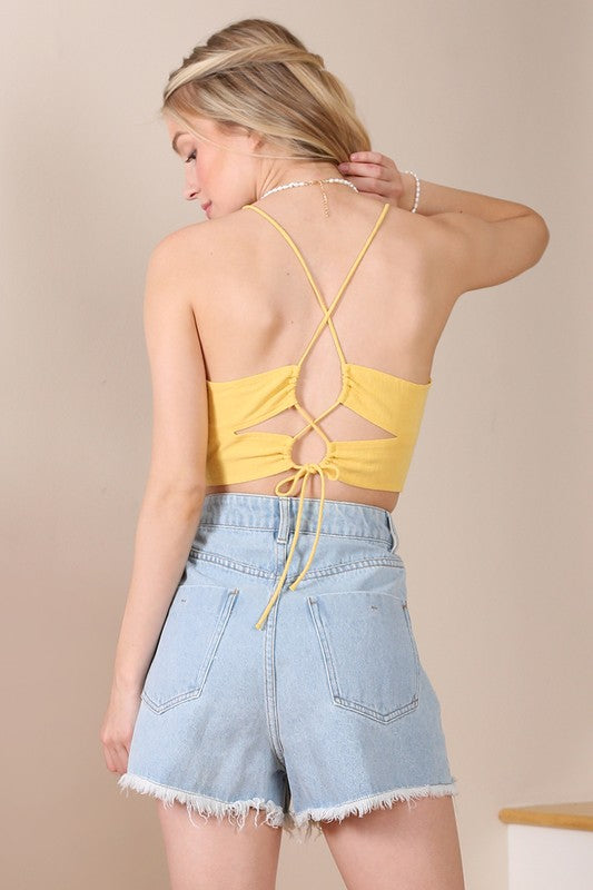 A person wearing an SL yellow crop tank top and denim shorts stands against a neutral background.