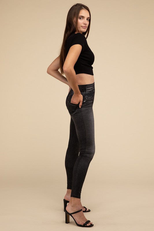 A person wearing Denim Leggings in a high-waisted black design and paired with black heels poses against a plain beige background, highlighting the sleek, stretchy fit.