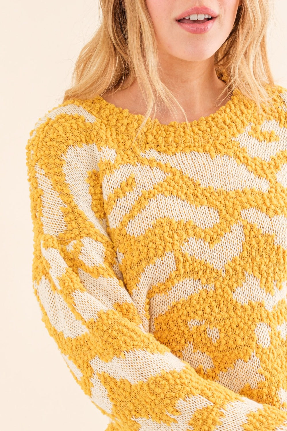 A person with long hair wearing a stylish yellow and white And The Why Full Size Textured Pattern Contrast Sweater and blue jeans stands against a beige background.