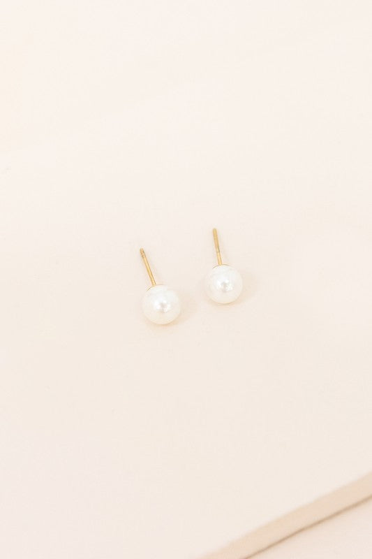 Flawless Pearl Stud Earrings - Small feature elegant pearl studs set on sleek 14k gold-plated posts, displayed against a light cream background.