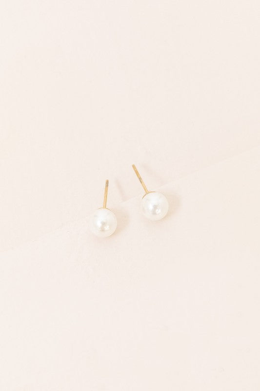 Flawless Pearl Stud Earrings - Small feature elegant pearl studs set on sleek 14k gold-plated posts, displayed against a light cream background.