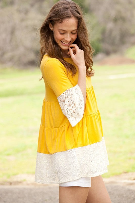 A woman wearing a Plus Lace Trim Tiered Tunic with striped design and lace details on the sleeves and hem stands in front of a plain beige background. She is also wearing ripped jeans.