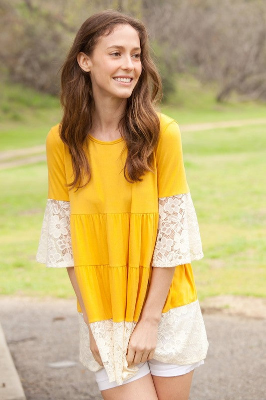 A woman wearing a Plus Lace Trim Tiered Tunic with striped design and lace details on the sleeves and hem stands in front of a plain beige background. She is also wearing ripped jeans.