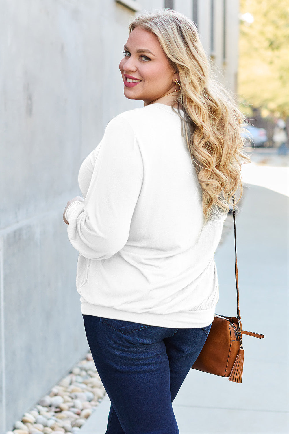 A woman with brown hair is standing against a concrete wall, wearing the Basic Bae Full Size V-Neck Lantern Sleeve Top in teal and blue basic-style jeans, smiling.