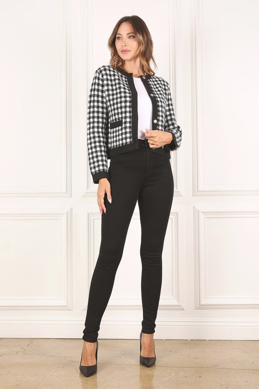 A woman dressed in the Black Check Knitted Jacket, featuring snap buttons and functional pockets, complemented by black pants, stands against a white background.