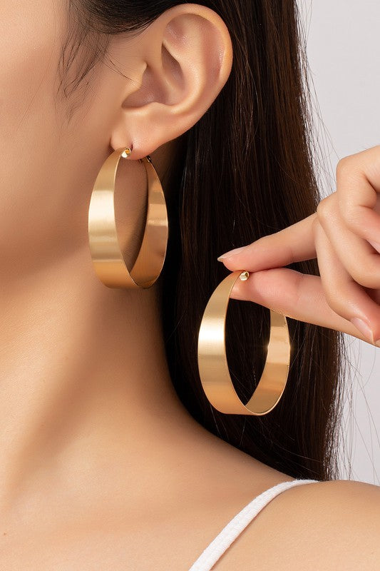 Four Satin Surface Wide Hoop Earrings are displayed on a beige and satin background. Two earrings feature a silver finish, while the other two are gold-plated. Each pair is arranged parallel to one another.