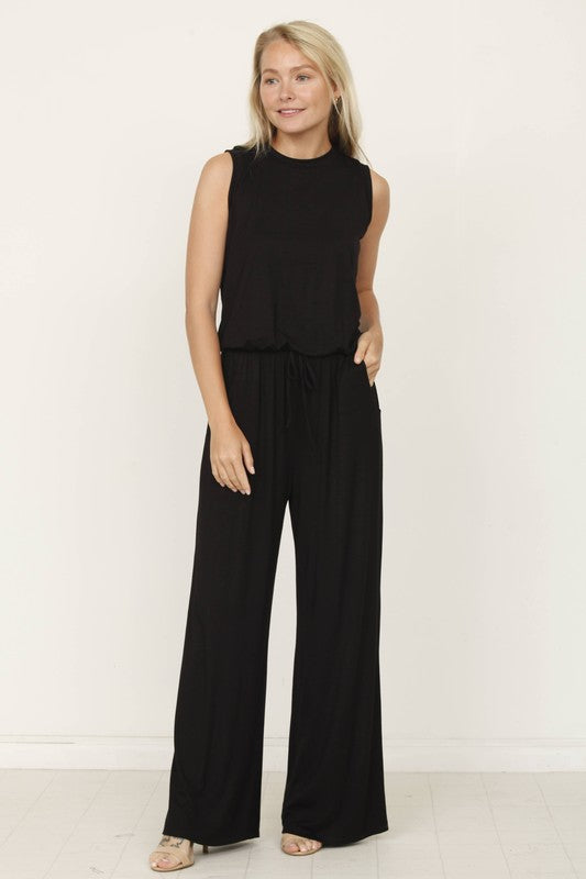 A person poses indoors against a white background, wearing the Plus Solid Drawstring Pocket Jumpsuit in a sleek olive green, crafted from soft rayon with a stylish drawstring detail.