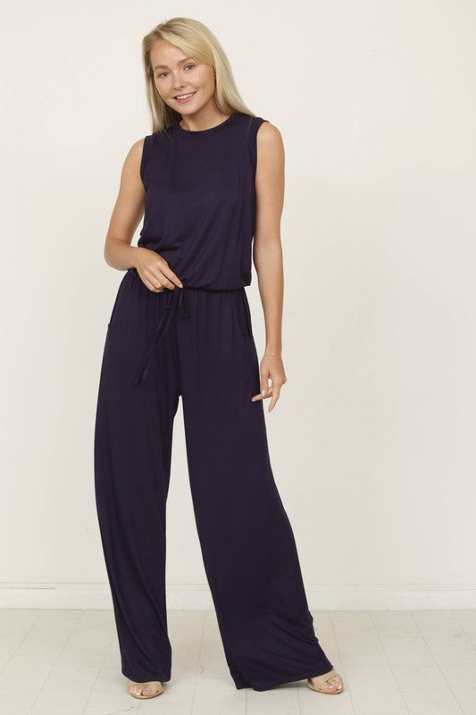 A person poses indoors against a white background, wearing the Plus Solid Drawstring Pocket Jumpsuit in a sleek olive green, crafted from soft rayon with a stylish drawstring detail.