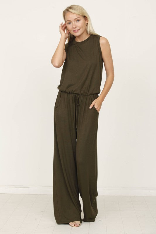 A person poses indoors against a white background, wearing the Plus Solid Drawstring Pocket Jumpsuit in a sleek olive green, crafted from soft rayon with a stylish drawstring detail.