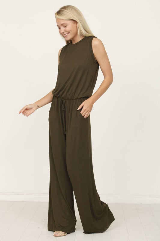 A person poses indoors against a white background, wearing the Plus Solid Drawstring Pocket Jumpsuit in a sleek olive green, crafted from soft rayon with a stylish drawstring detail.