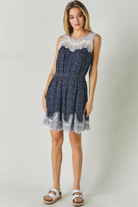 A woman wearing the Printed Sleeveless Lace Trim Mini Dress is seated against a light background.