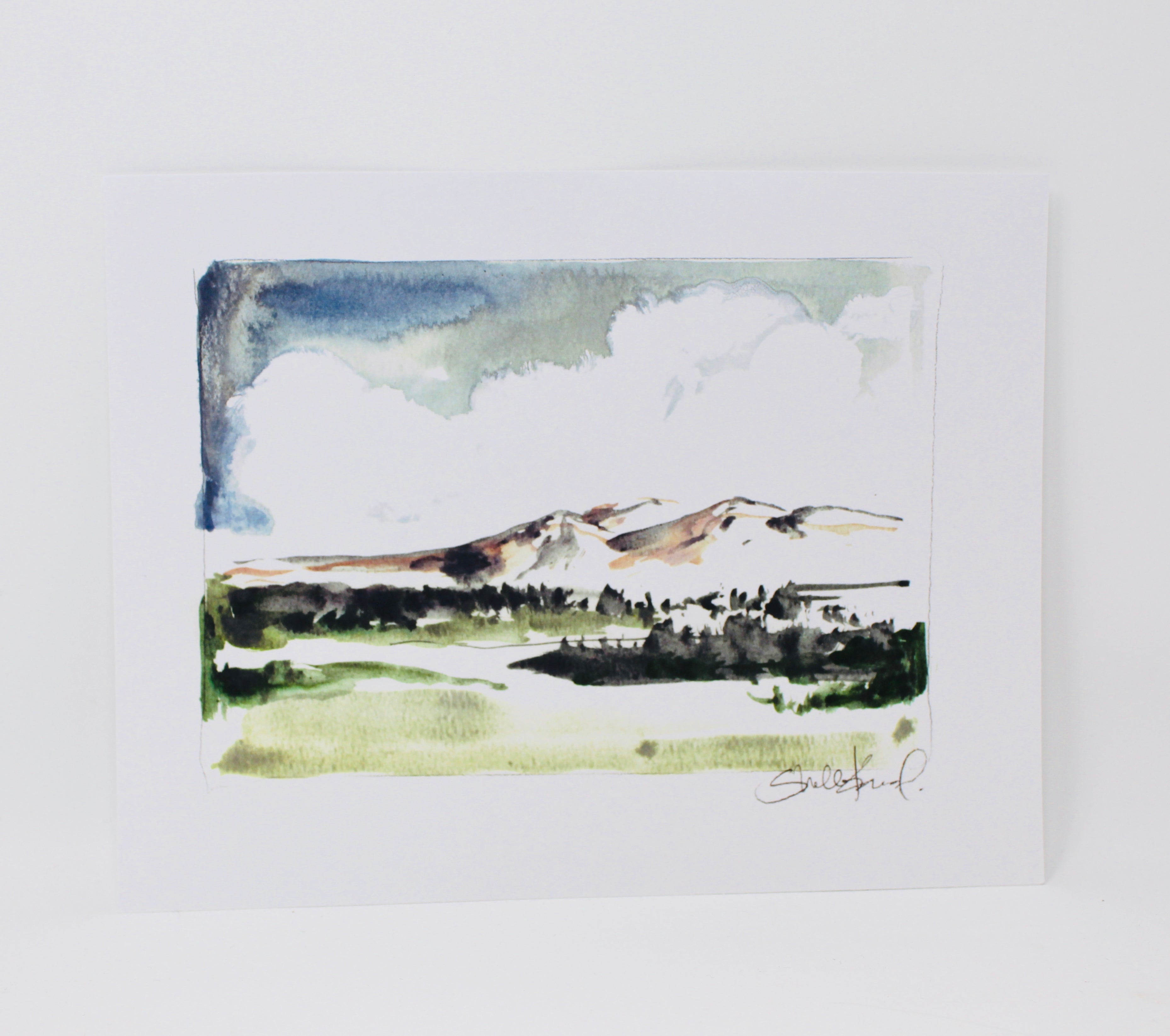 The "Mountain Landscape 11x14 Print" captures a simple impressionistic watercolor scene of green fields, lush trees, and a majestic mountain range beneath a cloudy sky, perfect for home decor and wall art.