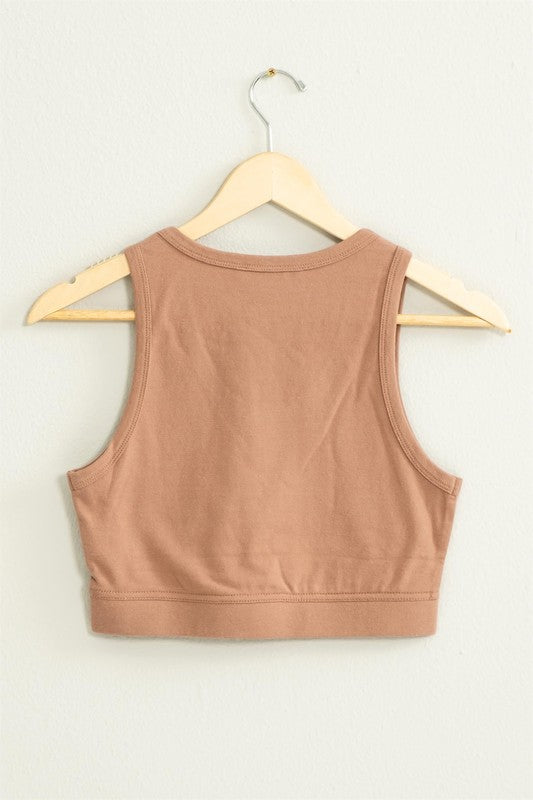 The "All I Need Cropped Tank Top," featuring a light blue hue and a fitted silhouette, hangs on a wooden hanger against a white wall.