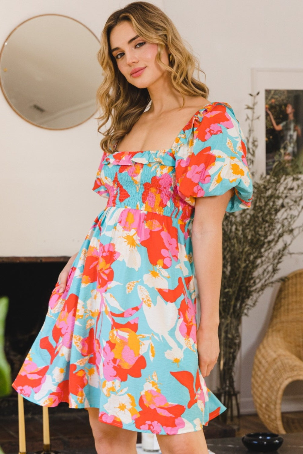 A woman wearing an ODDI Printed Smocked Puff Sleeve Mini Dress poses in a room decorated with a mirror and framed art on the wall.