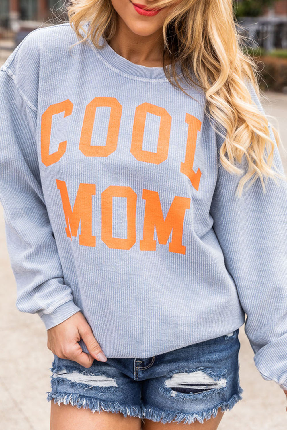 A person with long blonde hair stands facing away, wearing a Gray Cool Mom Graphic Print Cording Sweatshirt and blue jeans.